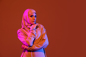 Image showing Beautiful arab woman posing in stylish hijab isolated on brown studio background in neon light. Fashion, beauty, style concept