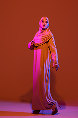 Image showing Beautiful arab woman posing in stylish hijab isolated on brown studio background in neon light. Fashion, beauty, style concept