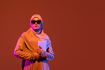 Image showing Beautiful arab woman posing in stylish hijab isolated on brown studio background in neon light. Fashion, beauty, style concept