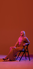 Image showing Beautiful arab woman posing in stylish hijab isolated on brown studio background in neon light. Fashion, beauty, style concept