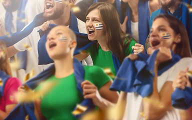 Image showing Uruguayan football, soccer fans cheering their team with a blue scarfs at stadium. Excited fans cheering a goal, supporting favourite players