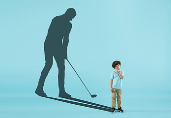 Image showing Childhood and dream about big and famous future. Conceptual image with boy and shadow of fit male sportive golf player on blue background