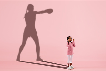 Image showing Childhood and dream about big and famous future. Conceptual image with girl and shadow of fit female boxer on coral pink background