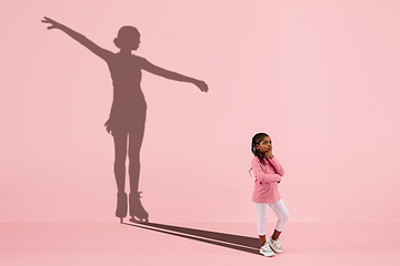 Image showing Childhood and dream about big and famous future. Conceptual image with girl and shadow of fit female figure skater on coral pink background