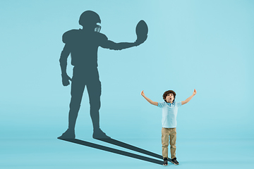 Image showing Childhood and dream about big and famous future. Conceptual image with boy and shadow of fit male football player on blue background