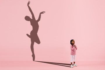 Image showing Childhood and dream about big and famous future. Conceptual image with girl and shadow of fit female ballet dancer on coral pink background