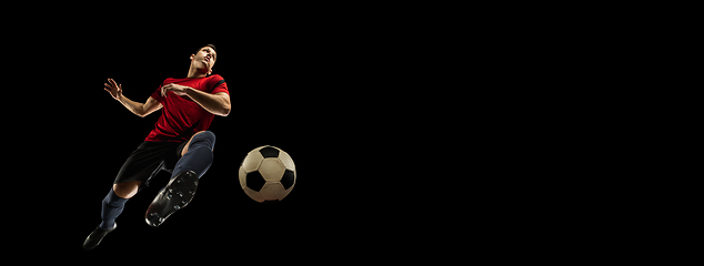 Image showing Young caucasian football, soccer player in action, motion isolated on black background, look from the bottom. Concept of sport, movement, energy and dynamic.