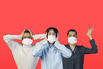 Image showing People in protective face masks isolated on red studio background. New rules of COVID spreading prevention