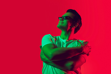 Image showing Caucasian man\'s portrait isolated on red studio background in multicolored neon light