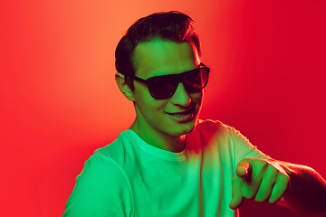 Image showing Caucasian man\'s portrait isolated on red studio background in multicolored neon light