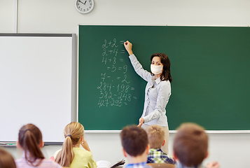 Image showing teacher in mask writing on chalkboard at school