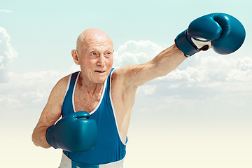 Image showing Senior man wearing sportwear boxing on sky background. Concept of sport, activity, movement, wellbeing. Copyspace, ad.