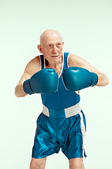 Image showing Senior man wearing sportwear boxing on sky background. Concept of sport, activity, movement, wellbeing. Copyspace, ad.