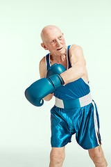 Image showing Senior man wearing sportwear boxing isolated on studio background. Concept of sport, activity, movement, wellbeing. Copyspace, ad.