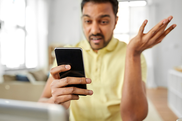 Image showing angry indian man with smartphone working at home