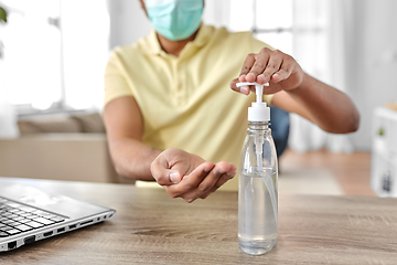 Image showing man in mask using hand sanitizer at home office