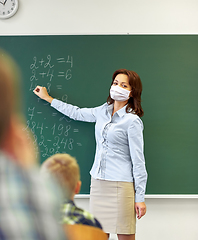 Image showing teacher in mask writing on chalkboard at school