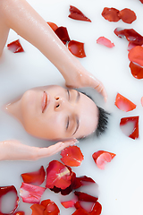 Image showing Close up female face in the milk bath with soft white glowing and rose petals. Copyspace for advertising. Beauty, fashion, style, bodycare concept.