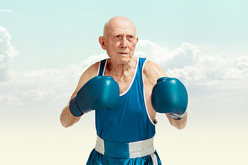 Image showing Senior man wearing sportwear boxing on sky background. Concept of sport, activity, movement, wellbeing. Copyspace, ad.