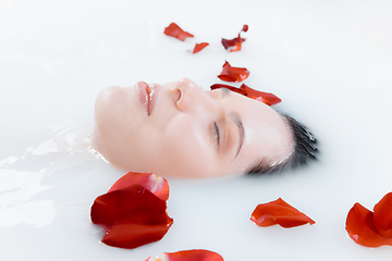Image showing Close up female face in the milk bath with soft white glowing and rose petals. Copyspace for advertising. Beauty, fashion, style, bodycare concept.