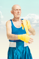 Image showing Senior man putting on sportwear for boxing on sky background. Concept of sport, activity, movement, wellbeing. Copyspace, ad.