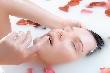 Image showing Close up female face in the milk bath with soft white glowing and rose petals. Copyspace for advertising. Beauty, fashion, style, bodycare concept.