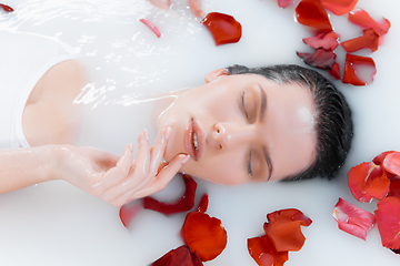 Image showing Close up female face in the milk bath with soft white glowing and rose petals. Copyspace for advertising. Beauty, fashion, style, bodycare concept.