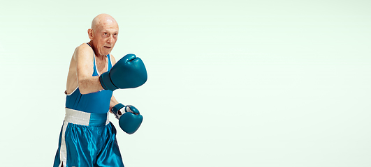 Image showing Senior man wearing sportwear boxing isolated on studio background. Concept of sport, activity, movement, wellbeing. Copyspace, ad.