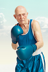 Image showing Senior man wearing sportwear boxing on sky background. Concept of sport, activity, movement, wellbeing. Copyspace, ad.