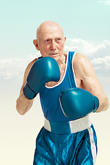 Image showing Senior man wearing sportwear boxing on sky background. Concept of sport, activity, movement, wellbeing. Copyspace, ad.