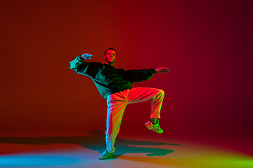 Image showing Stylish sportive boy dancing hip-hop in stylish clothes on colorful background at dance hall in neon light. Youth culture, movement, style and fashion, action.