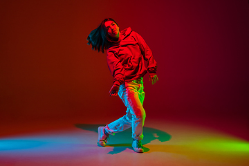 Image showing Stylish sportive girl dancing hip-hop in stylish clothes on colorful background at dance hall in neon light. Youth culture, movement, style and fashion, action.