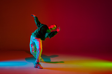 Image showing Stylish sportive boy dancing hip-hop in stylish clothes on colorful background at dance hall in neon light. Youth culture, movement, style and fashion, action.