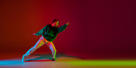 Image showing Stylish sportive boy dancing hip-hop in stylish clothes on colorful background at dance hall in neon light. Youth culture, movement, style and fashion, action.