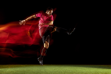 Image showing Young football, soccer player of team in action, motion isolated on black background in mixed neon light. Concept of sport, movement, energy and dynamic.