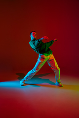 Image showing Stylish sportive boy dancing hip-hop in stylish clothes on colorful background at dance hall in neon light. Youth culture, movement, style and fashion, action.