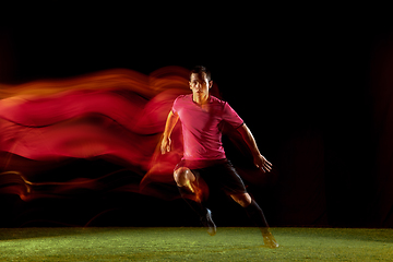 Image showing Young football, soccer player of team in action, motion isolated on black background in mixed neon light. Concept of sport, movement, energy and dynamic.