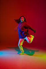 Image showing Stylish sportive girl dancing hip-hop in stylish clothes on colorful background at dance hall in neon light. Youth culture, movement, style and fashion, action.