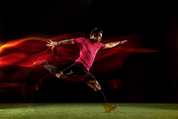 Image showing Young football, soccer player of team in action, motion isolated on black background in mixed neon light. Concept of sport, movement, energy and dynamic.