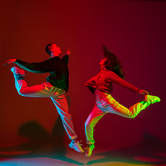 Image showing Stylish sportive couple dancing hip-hop in stylish clothes on colorful background at dance hall in neon light. Youth culture, movement, style and fashion, action.