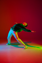 Image showing Stylish sportive boy dancing hip-hop in stylish clothes on colorful background at dance hall in neon light. Youth culture, movement, style and fashion, action.