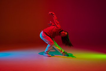 Image showing Stylish sportive girl dancing hip-hop in stylish clothes on colorful background at dance hall in neon light. Youth culture, movement, style and fashion, action.