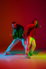 Image showing Stylish sportive couple dancing hip-hop in stylish clothes on colorful background at dance hall in neon light. Youth culture, movement, style and fashion, action.