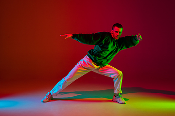 Image showing Stylish sportive boy dancing hip-hop in stylish clothes on colorful background at dance hall in neon light. Youth culture, movement, style and fashion, action.