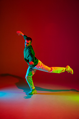 Image showing Stylish sportive boy dancing hip-hop in stylish clothes on colorful background at dance hall in neon light. Youth culture, movement, style and fashion, action.