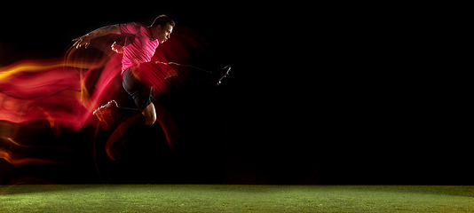 Image showing Young football, soccer player of team in action, motion isolated on black background in mixed neon light. Concept of sport, movement, energy and dynamic.