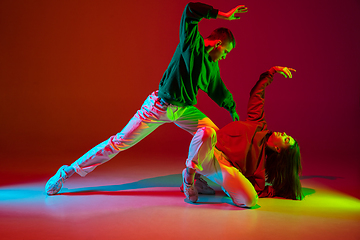 Image showing Stylish sportive couple dancing hip-hop in stylish clothes on colorful background at dance hall in neon light. Youth culture, movement, style and fashion, action.
