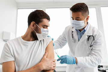 Image showing male doctor in mask giving vaccine to patient