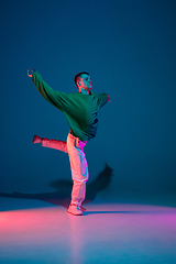 Image showing Stylish sportive boy dancing hip-hop in stylish clothes on colorful background at dance hall in neon light. Youth culture, movement, style and fashion, action.