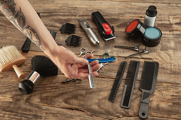 Image showing Hand of male barber with equipment set isolated on wooden table background.